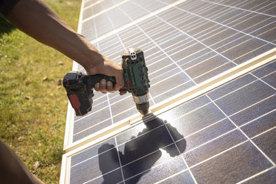 Hand of male engineer using drill on solar panels while working at power station