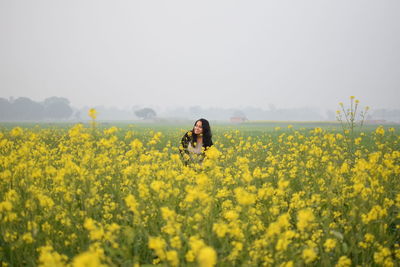 Portrait of young woman amidst yellow flowers on oilseed rape field