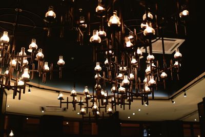 Low angle view of illuminated light bulbs hanging at night