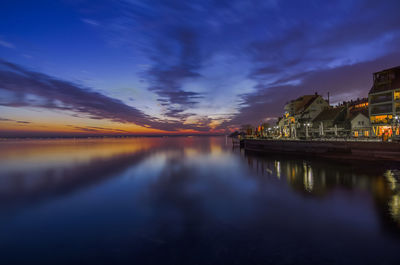 Scenic view of lake by buildings against sky at sunset