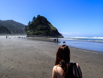 Rear view of woman walking on beach against clear blue sky