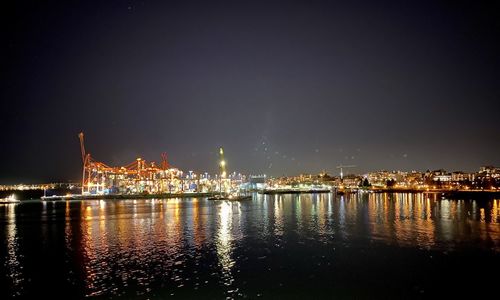 Illuminated city by river against sky at night