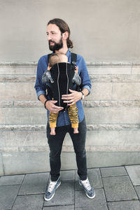 Full length of mid adult father carrying baby in carrier on sidewalk