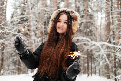 Portrait of young woman holding sparkler against trees