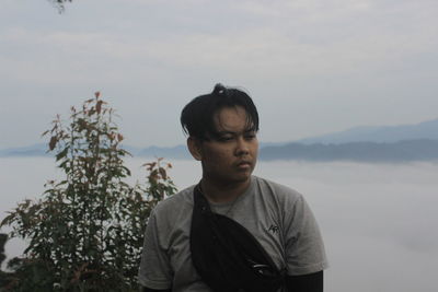 Portrait of young man looking at mountains against sky