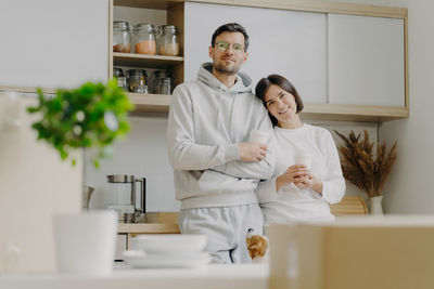 Low angle portrait of couple holding coffee standing in kitchen