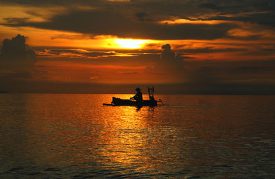 Silhouette man in boat on sea against cloudy sky during sunset