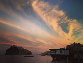 Buildings by sea against sky during sunset