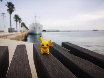Close-up of yellow toy on bench by sea against sky
