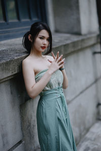 Portrait of young woman standing against wall