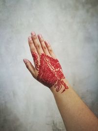 Cropped hand of woman with henna tattoo against wall