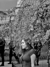 Portrait of young woman standing by flowering tree