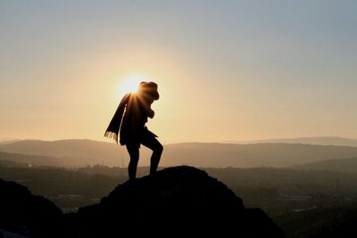 Silhouette person standing on mountain against clear sky during sunset