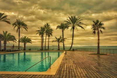 Palm trees by swimming pool against sky during sunset