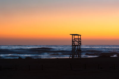 Silhouette lifeguard hut on beach against sky during sunset