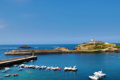 Boats moored in sea against clear blue sky