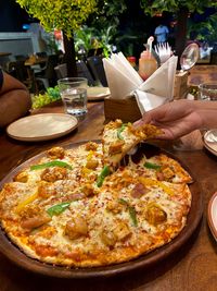 Cropped image of hand holding pizza on table