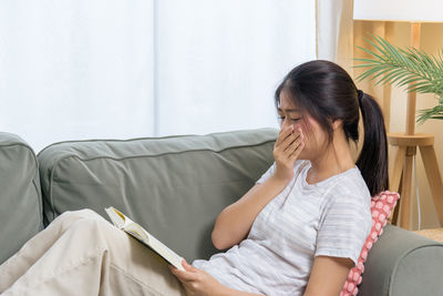 Side view of young woman sitting on sofa at home