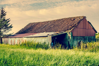 Barn on field by houses against sky
