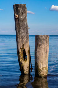 Wooden posts on sea against sky