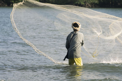 Rear view of fisherman throwing net in lake