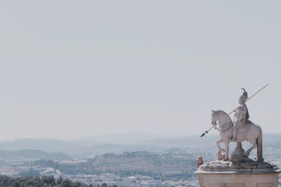 Statue by city against clear sky