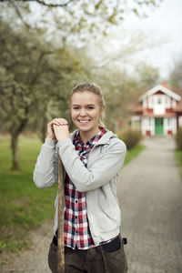 Portrait of smiling teenage girl holding pitchfork while standing on footpath