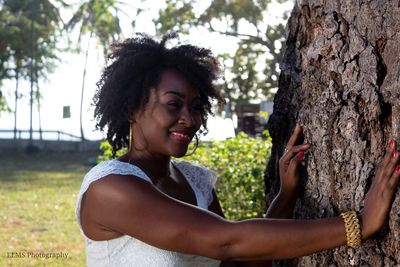 Portrait of smiling young woman against tree trunk