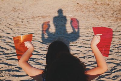 Rear view of woman holding colorful plastic paper at beach during sunny day