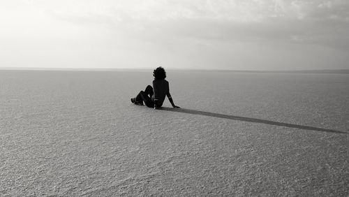 Rear view of woman sitting on salt flat against sky