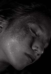Close-up of woman with glitter against black background