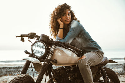 Woman with head in hand sitting on motor cycle at beach