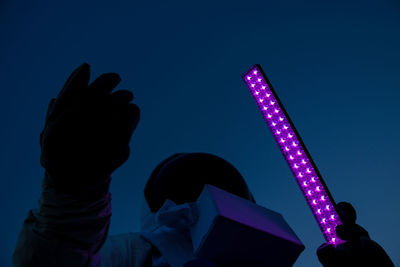 Low angle view of person in astronaut costume holding illuminated light against sky