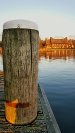 Wooden bollard on pier in lake against sky