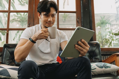 Young man using mobile phone while sitting on window