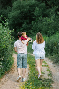 Happy young family with their son in their arms are walking along a forest path and enjoying