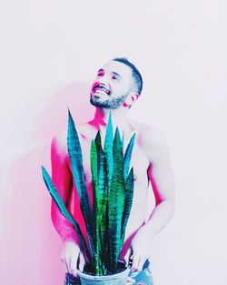 Smiling shirtless man holding potted plant standing against pink background