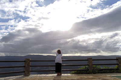 Rear view of man standing on pier over lake against sky