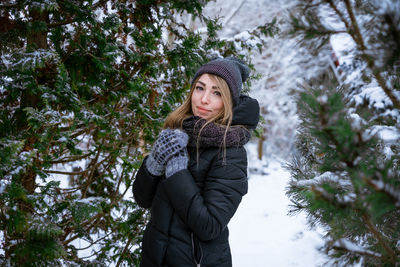 Portrait of young woman standing by tree during winter