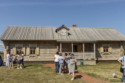 People outside house on field against clear sky