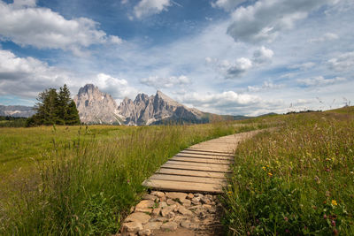 Wooden hiking trail at seiser alm with sassolungo mountain group in front of blue sky with clouds