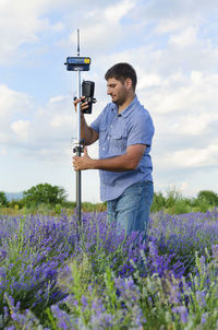 Surveyor using equipment on lavender field against cloudy sky