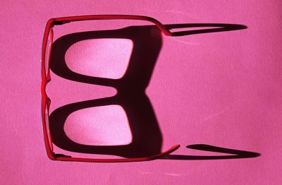 Close-up of eyeglasses on table against pink background