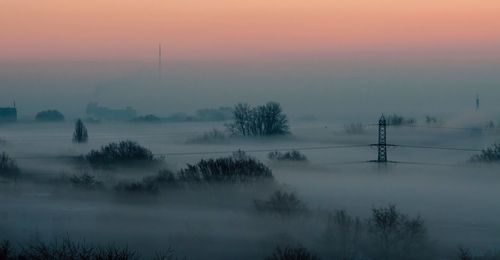 Scenic view of trees in foggy weather against sky during sunset