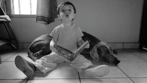 Portrait of cute baby boy puckering lips while sitting by dog on floor at home