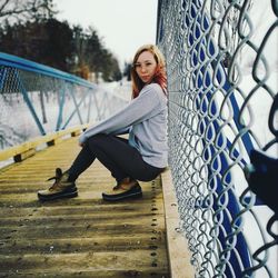 Young woman sitting on chainlink fence