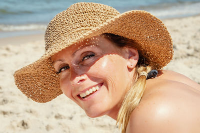 Close-up portrait of smiling woman in hat at beach