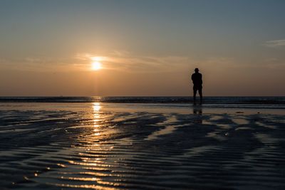 Silhouette man standing on beach against sky during sunset