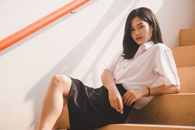 Portrait of young woman sitting against white wall