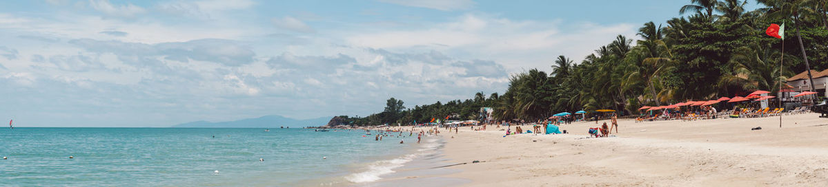 People at beach against cloudy sky during sunny day